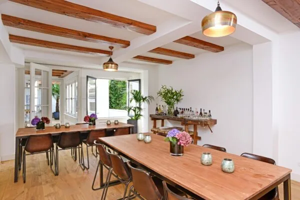 Stijlvol ingerichte eetruimte aan de Nieuwe Kerkstraat met houten tafels, bloemen, en een drankentafel bij een open raam.